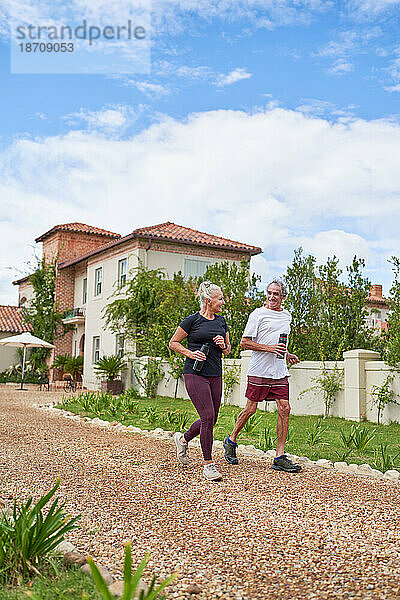 Glückliches älteres Paar joggt auf Fußweg vor der Sommervilla