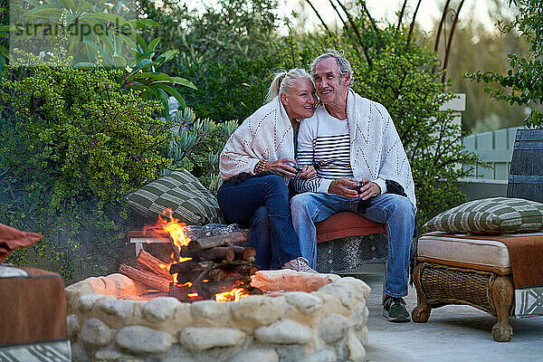 Glückliches älteres Paar sitzt und trinkt Wein an der Feuerstelle auf der Terrasse