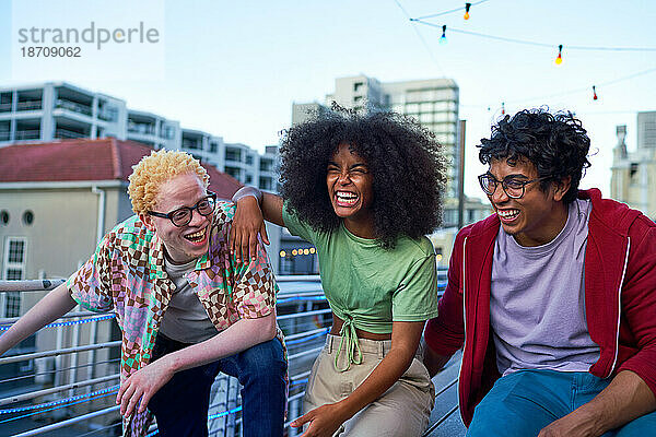 Fröhliche junge Freunde lachen auf dem Balkon einer Stadtwohnung
