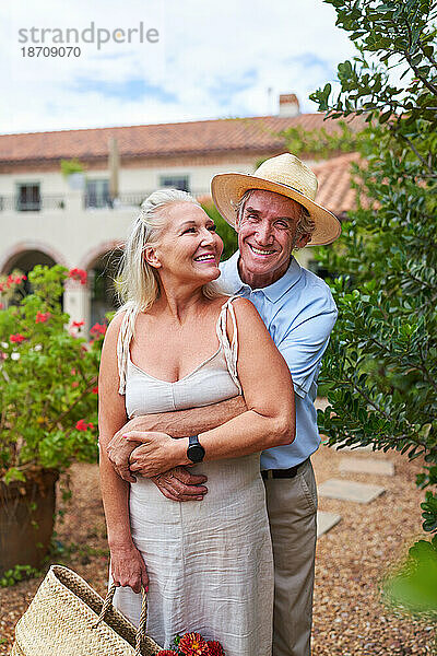 Porträt eines glücklichen älteren Paares  das sich vor der Sommervilla umarmt
