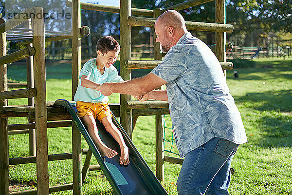 Vater spielt mit Sohn mit Down-Syndrom auf Rutsche im sonnigen Hinterhof