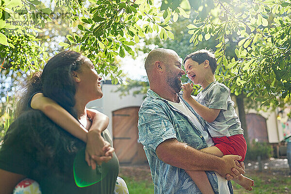 Glückliche Eltern und Sohn mit Down-Syndrom unter sonnigem Baum