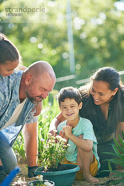 Glücklicher Junge mit Down-Syndrom pflanzt mit seiner Familie Blumen im Garten