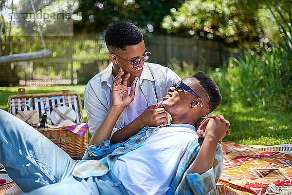 Fröhliches junges schwules Männerpaar kuschelt und genießt Picknick im Park