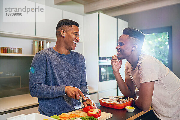 Glückliches junges schwules männliches Paar  das zu Hause Gemüse in der Küche kocht