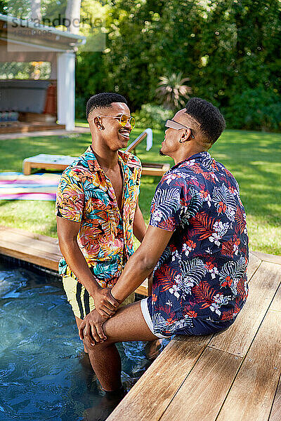 Glückliches junges schwules männliches Paar im Sommerschwimmbad im Hinterhof
