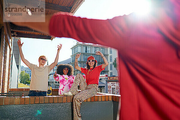 Fröhliche junge Freunde jubeln auf dem sonnigen  städtischen Wohnungsbalkon