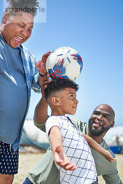 Glückliches schwules männliches Paar und Sohn spielen mit Fußball am sonnigen Strand