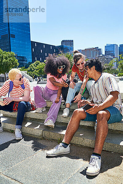 Junge Freunde hängen mit Smartphones im sonnigen Stadtpark herum