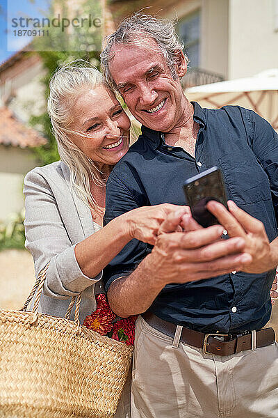 Glückliches Seniorenpaar nutzt Smartphone auf sonniger Terrasse