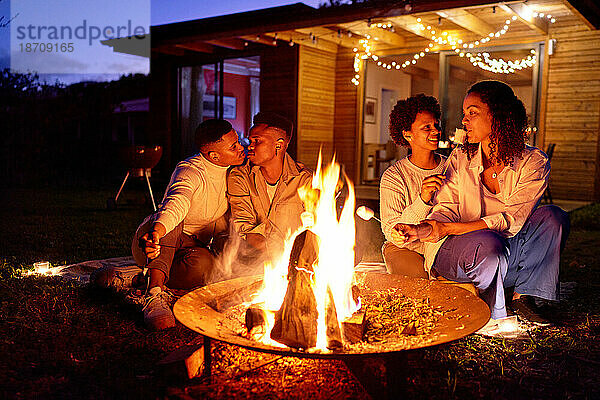 Glückliche schwule Paare rösten Marshmallows an der Feuerstelle im sommerlichen Hinterhof