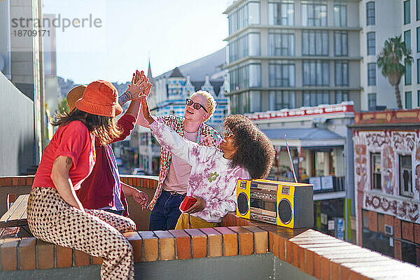 Fröhliche junge Freunde beim High-Five auf dem sonnigen Balkon der Stadt