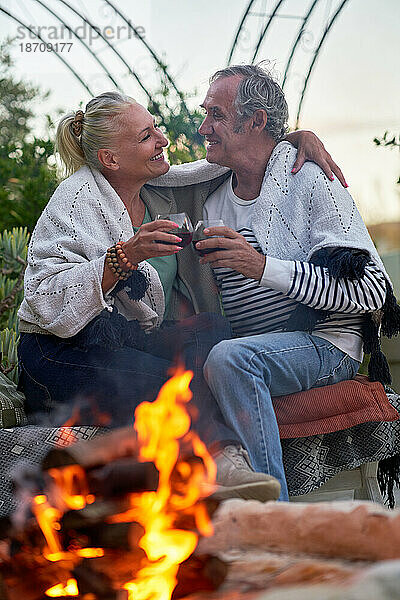 Glückliches älteres Paar umarmt sich und trinkt Rotwein an der Feuerstelle auf der Terrasse
