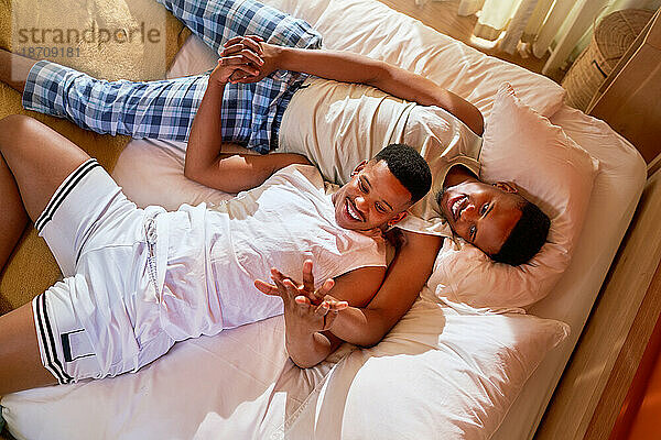 Glückliches junges schwules männliches Paar kuschelt und hält Händchen auf dem Bett