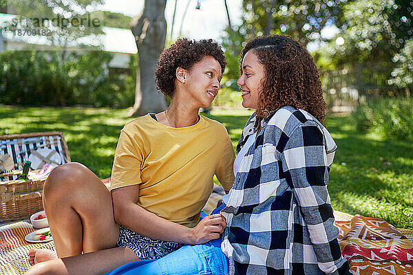 Glückliches lesbisches Paar unterhält sich auf einer Picknickdecke im Sommerpark