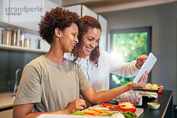 Glückliches lesbisches Paar kocht mit einem digitalen Tablet und schaut sich das Rezept an