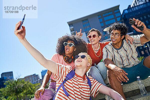 Fröhliche junge Freunde machen Selfie im sonnigen Stadtpark