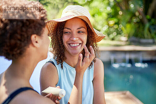 Glückliches  verspieltes lesbisches Paar  das am Pool Sonnencreme auf die Nase aufträgt