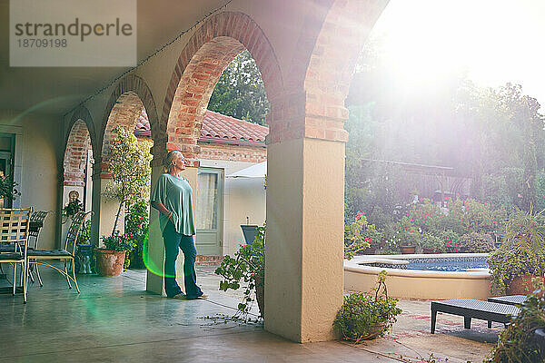 Ruhige  nachdenkliche Seniorin steht auf der sonnigen Villa-Terrasse