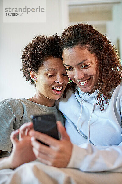 Glückliches lesbisches Paar  das zu Hause gemeinsam sein Smartphone nutzt