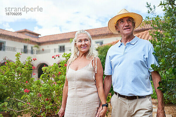 Porträt eines glücklichen älteren Paares  das im Garten vor der Villa spaziert