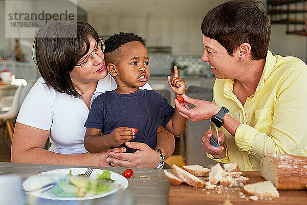 Lesbisches Paar und Sohn unterhalten sich und essen Tomaten am Esstisch