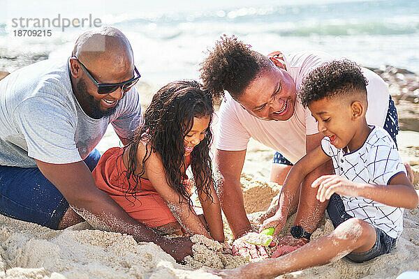 Glückliches schwules männliches Paar mit Kindern  die am sonnigen Strand im Sand spielen
