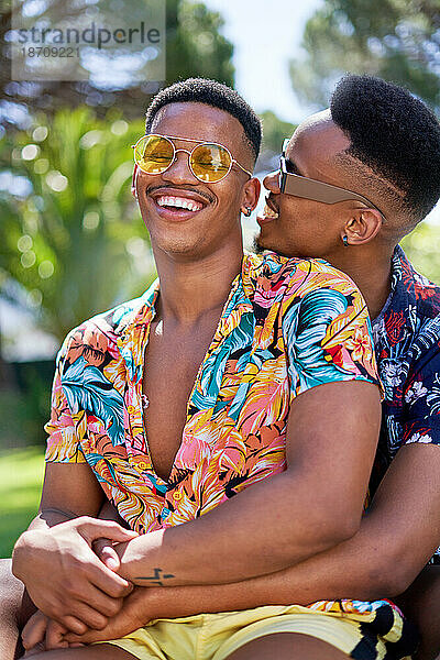 Glückliches junges schwules männliches Paar mit Sonnenbrille  das sich umarmt und lacht