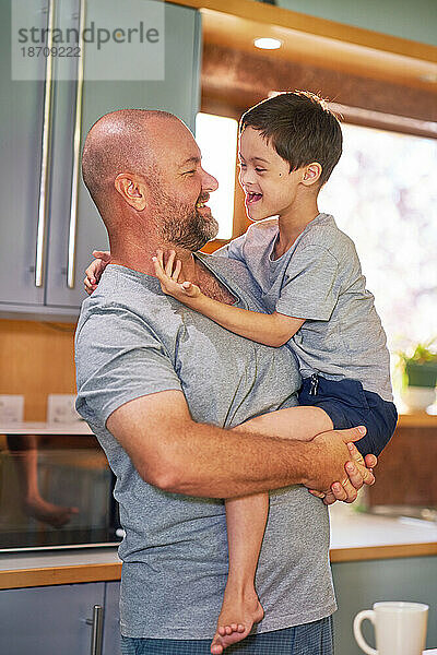 Vater hält glücklichen  süßen Sohn mit Down-Syndrom in der Küche