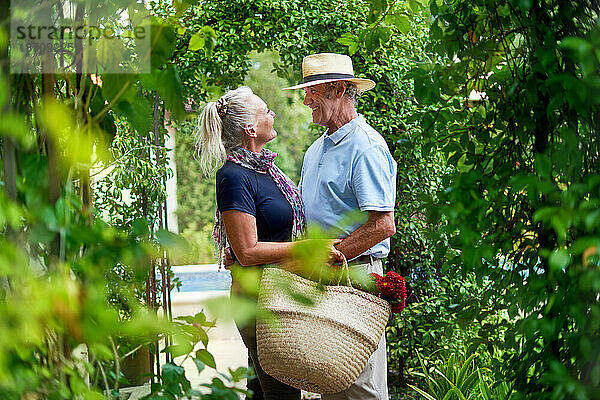 Glückliches Seniorenpaar umarmt sich unter üppigem grünem Spalier im Sommergarten