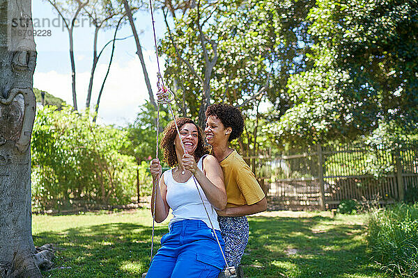 Glückliches lesbisches Paar spielt auf Schaukel im sonnigen Sommerpark
