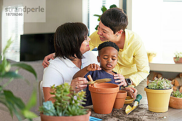 Glückliches lesbisches Paar und Sohn pflanzen zu Hause Pflanzen in Blumentöpfe