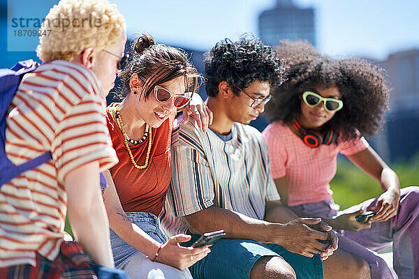 Junge Freunde nutzen Smartphones in der sonnigen Stadt