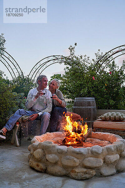 Glückliches älteres Paar trinkt Wein an der Feuerstelle auf der Sommerterrasse