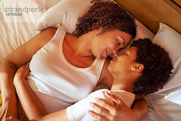 Liebevolles lesbisches Paar  das sich von Angesicht zu Angesicht auf dem Bett kuschelt