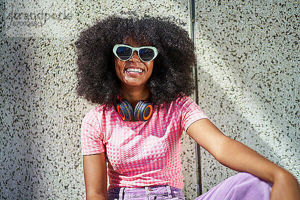 Porträt einer glücklichen jungen Frau mit Sonnenbrille und Kopfhörern