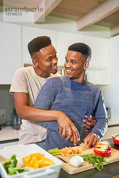Fröhliches  liebevolles junges schwules Männerpaar  das zu Hause kocht und sich umarmt