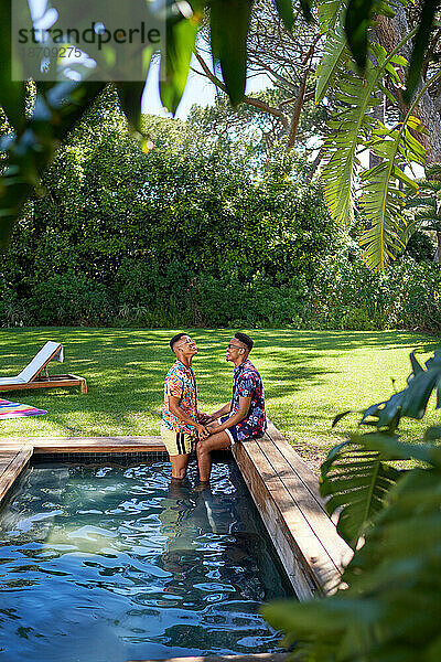 Junges schwules männliches Paar entspannt sich im Sommer im Hinterhof am Pool