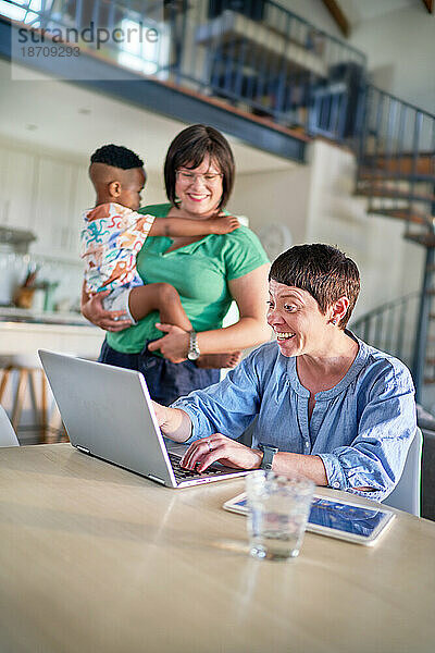 Glückliches lesbisches Paar mit Sohn  der zu Hause im Esszimmer einen Laptop benutzt