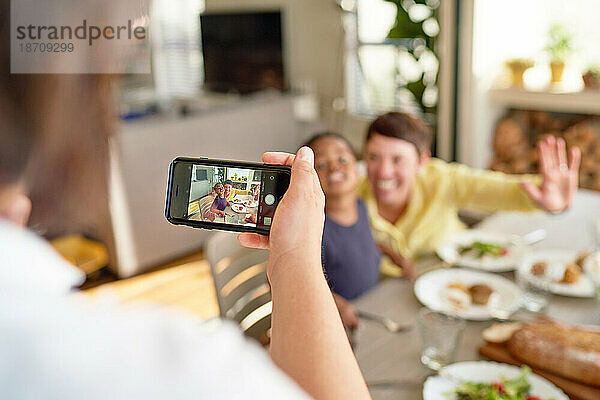 Frau mit Kameratelefon fotografiert Frau und Sohn am Esstisch