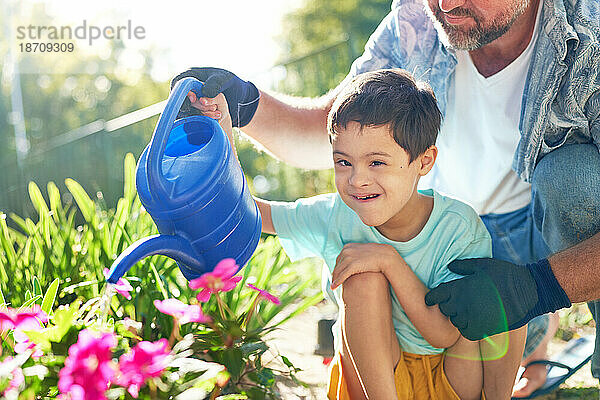 Porträt eines glücklichen Jungen mit Down-Syndrom  der mit seinem Vater Blumen gießt