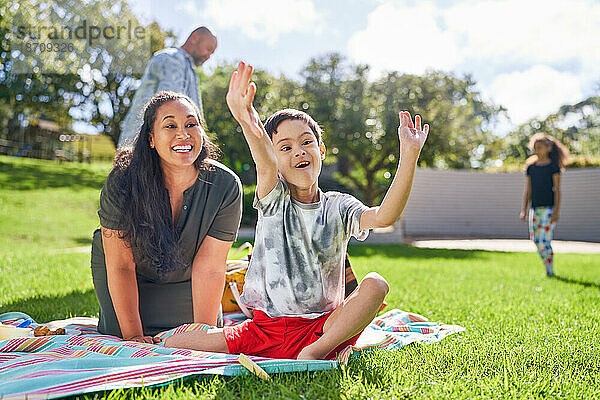 Glückliche Mutter beobachtet süßen Sohn mit Down-Syndrom beim Essen im Park