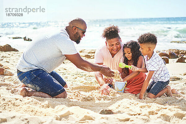 Schwules männliches Paar mit Kindern  die im Sand am sonnigen Meeresstrand spielen