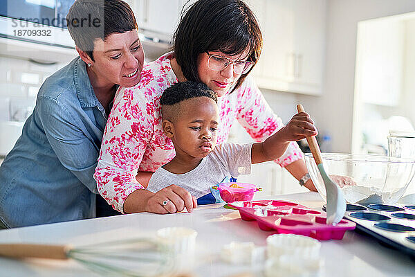 Lesbisches Paar und Sohn backen herzförmige Cupcakes in der Küche