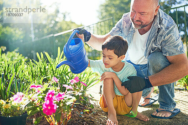 Vater und Sohn mit Down-Syndrom gießen Blumen im sonnigen Garten