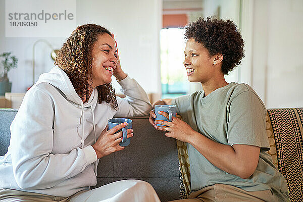 Glückliches lesbisches Paar trinkt Kaffee auf dem Sofa im Wohnzimmer zu Hause