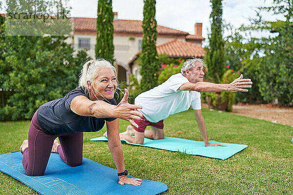 Glückliches älteres Paar  das Yoga im Gartengras der Villa praktiziert