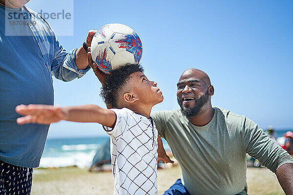 Schwules männliches Paar und Sohn spielen mit Fußball am sonnigen Strand