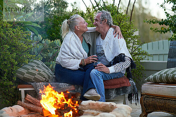 Glückliches älteres Paar  das Wein trinkt und sich an der Feuerstelle auf der Terrasse umarmt