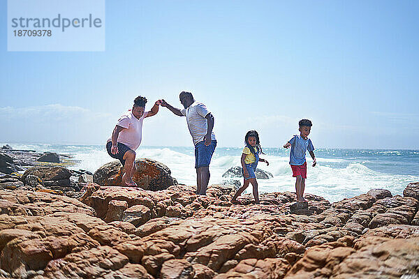 Homosexuelles männliches Paar und Kinder  die auf sonnigen Strandfelsen am Meer spazieren